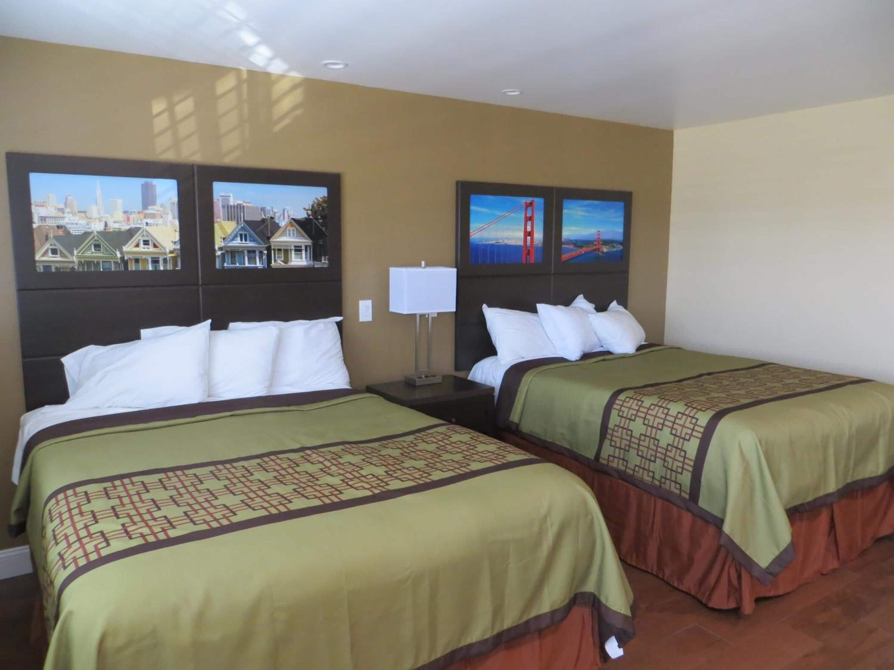 A hotel room with two beds, a nightstand, a lamp, and cityscape pictures on the wall.