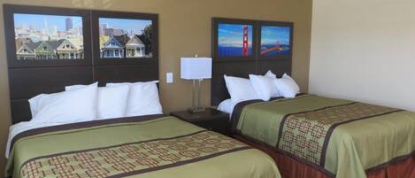 A hotel room with two beds, a nightstand, a lamp, and cityscape pictures on the wall.