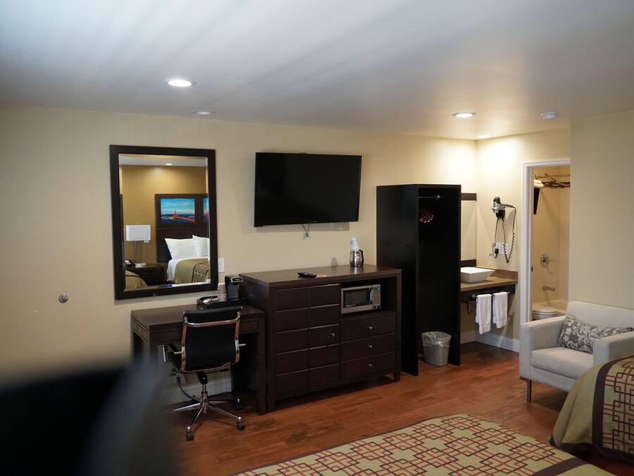 A hotel room with a bed, a desk with a chair, a television, a wardrobe, a bathroom with a shower, and a mirror.