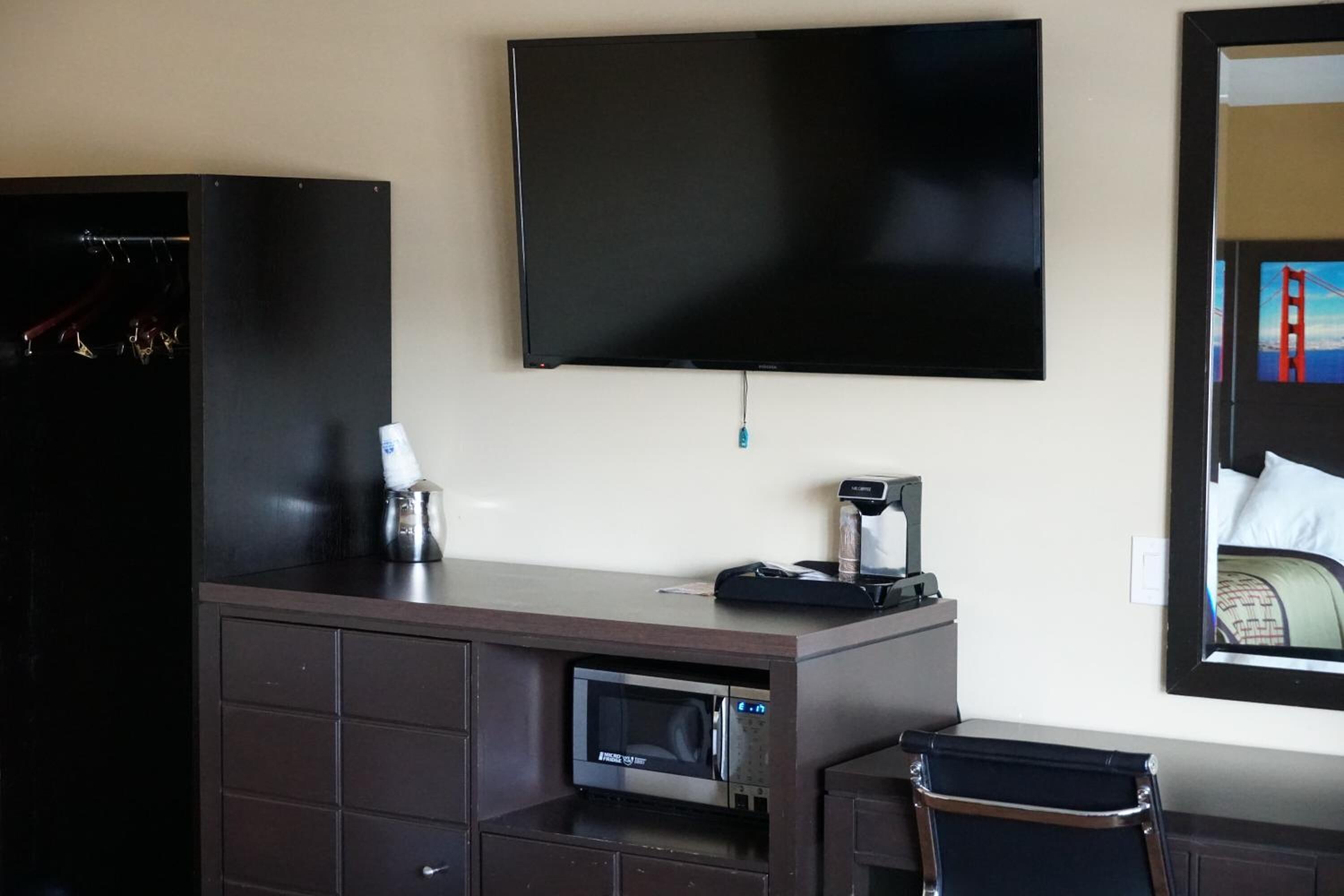 Habitación de hotel con televisor de pantalla plana en la pared, minibar, microondas y una maleta sobre un escritorio.