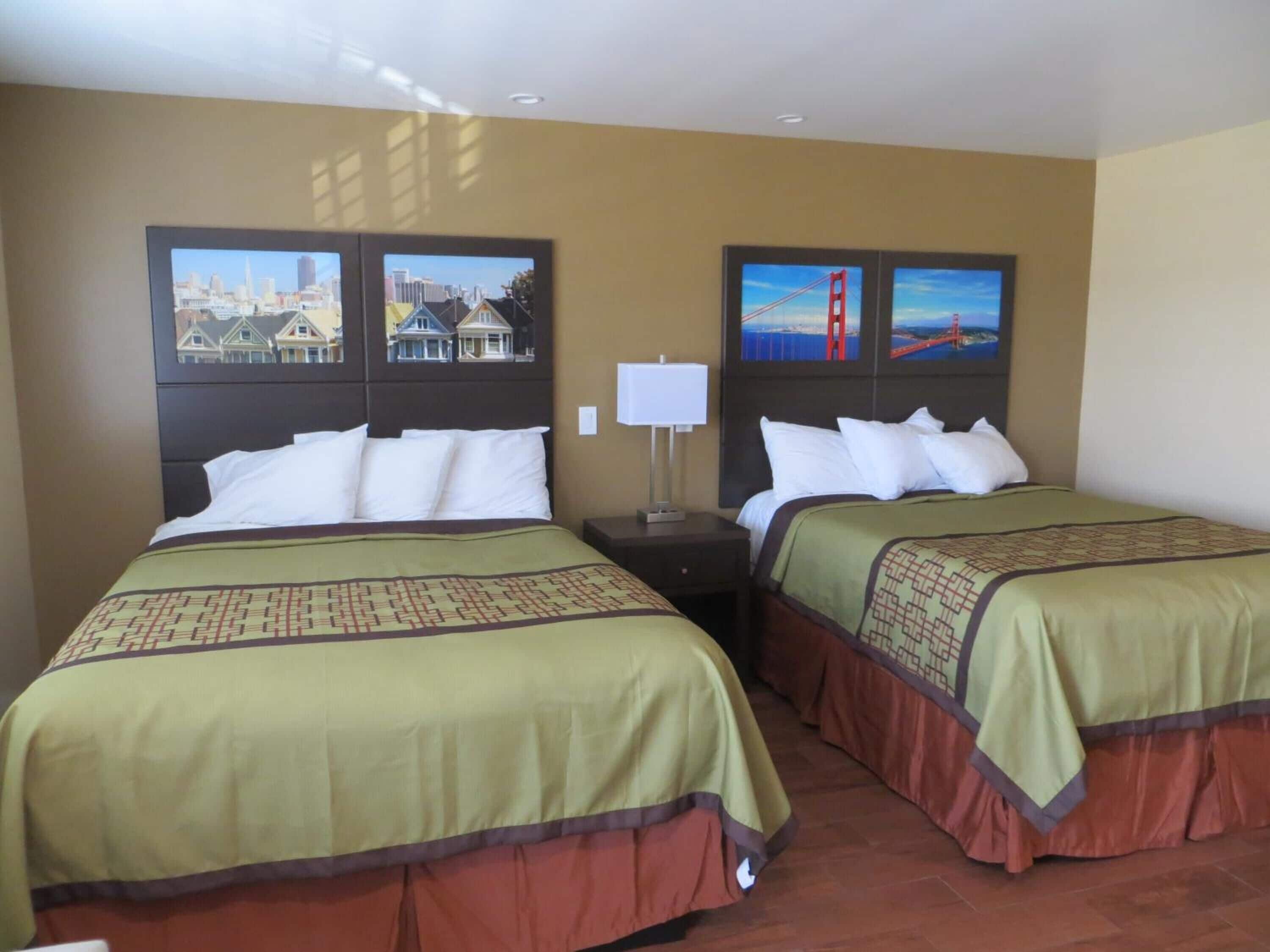 Camera d'albergo con due letti, ciascuno con una coperta e dei cuscini a motivi decorativi. Sulla parete, due quadri: uno raffigurante un paesaggio urbano e l'altro il Golden Gate Bridge.