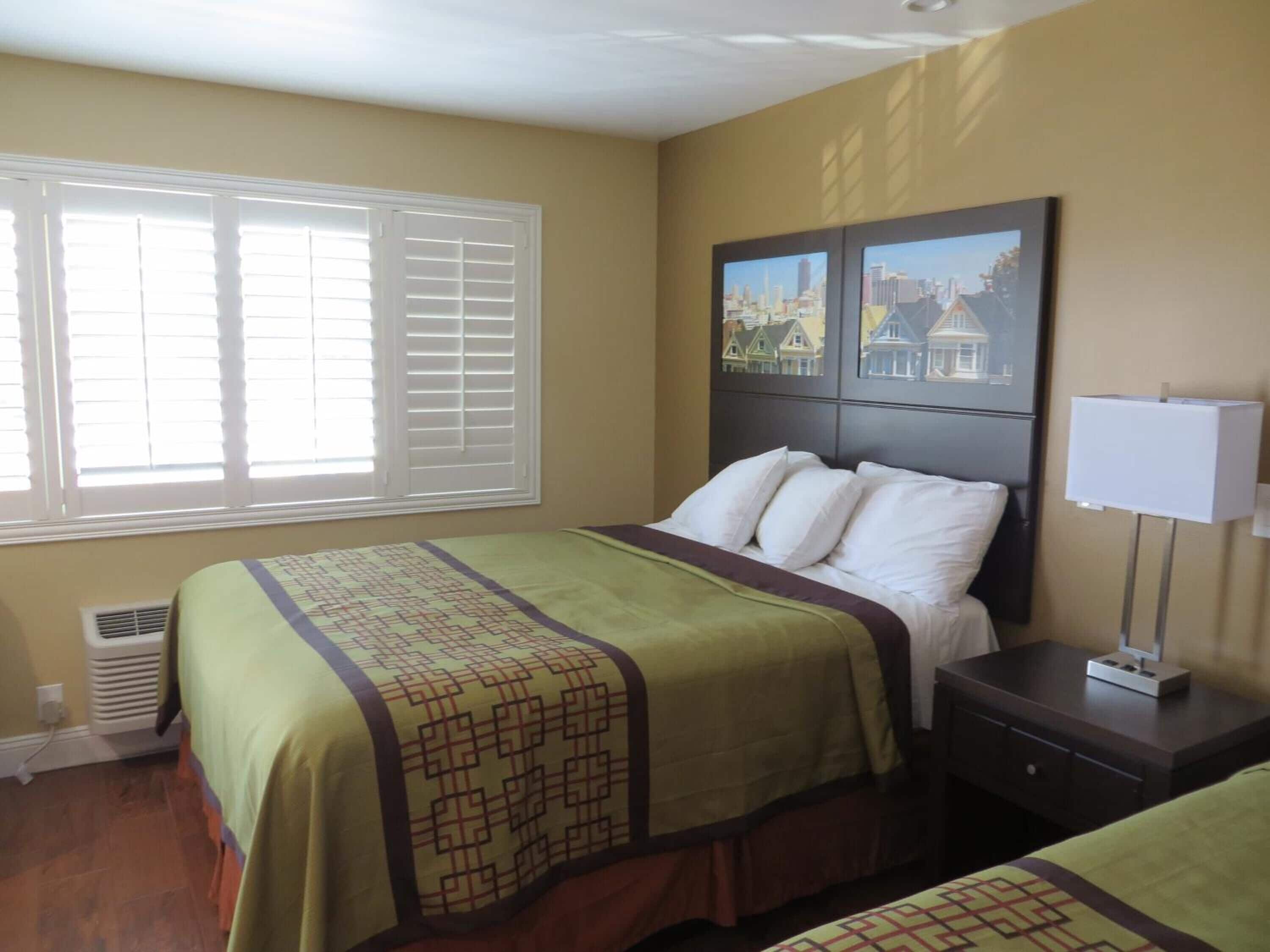 A hotel room with a bed, a nightstand, a window with blinds, and a wall-mounted picture.