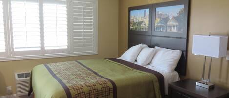 A hotel room with a bed, a nightstand, a window with blinds, and a wall-mounted picture.