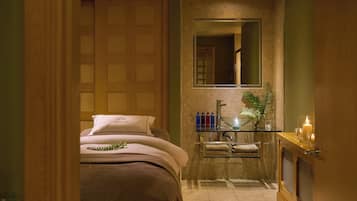 A hotel room with a bed, a glass shelf with toiletries, a mirror, and a plant.