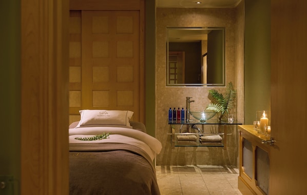 A hotel room with a bed, a glass shelf with toiletries, a mirror, and a plant.