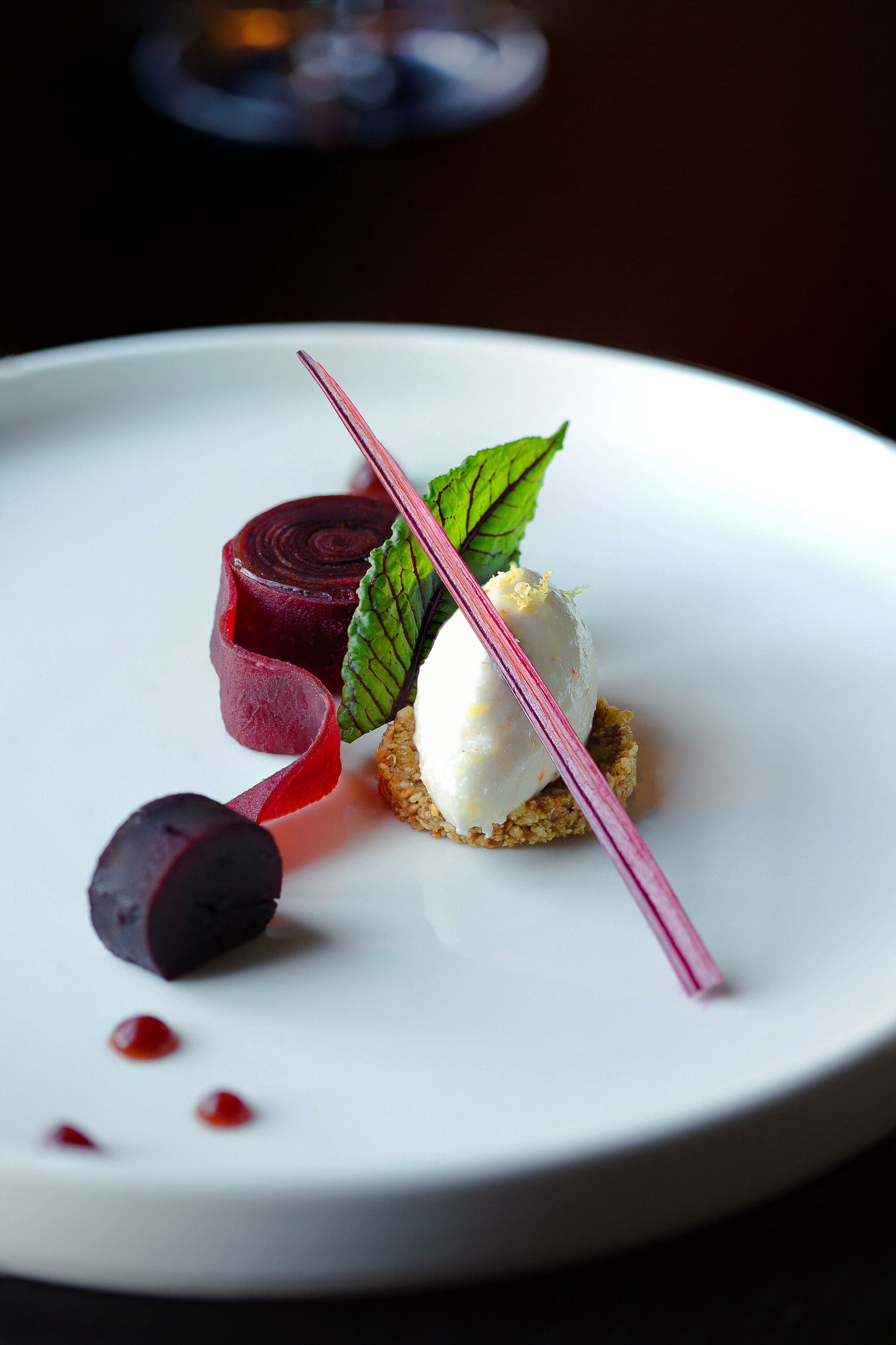 A dessert plate with a beet slice, ice cream, and a mint leaf.