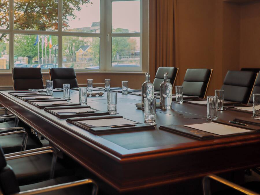 Un salón de conferencias con una larga mesa, sillas, botellas de agua y vasos.