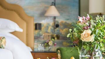 A hotel room with a bed, a vase with flowers, and a table with snacks.