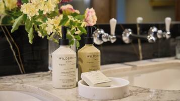 Dos botellas de jabón de manos y cuerpo Wildsmith Skin sobre una encimera de mármol, con un florero de flores al fondo.