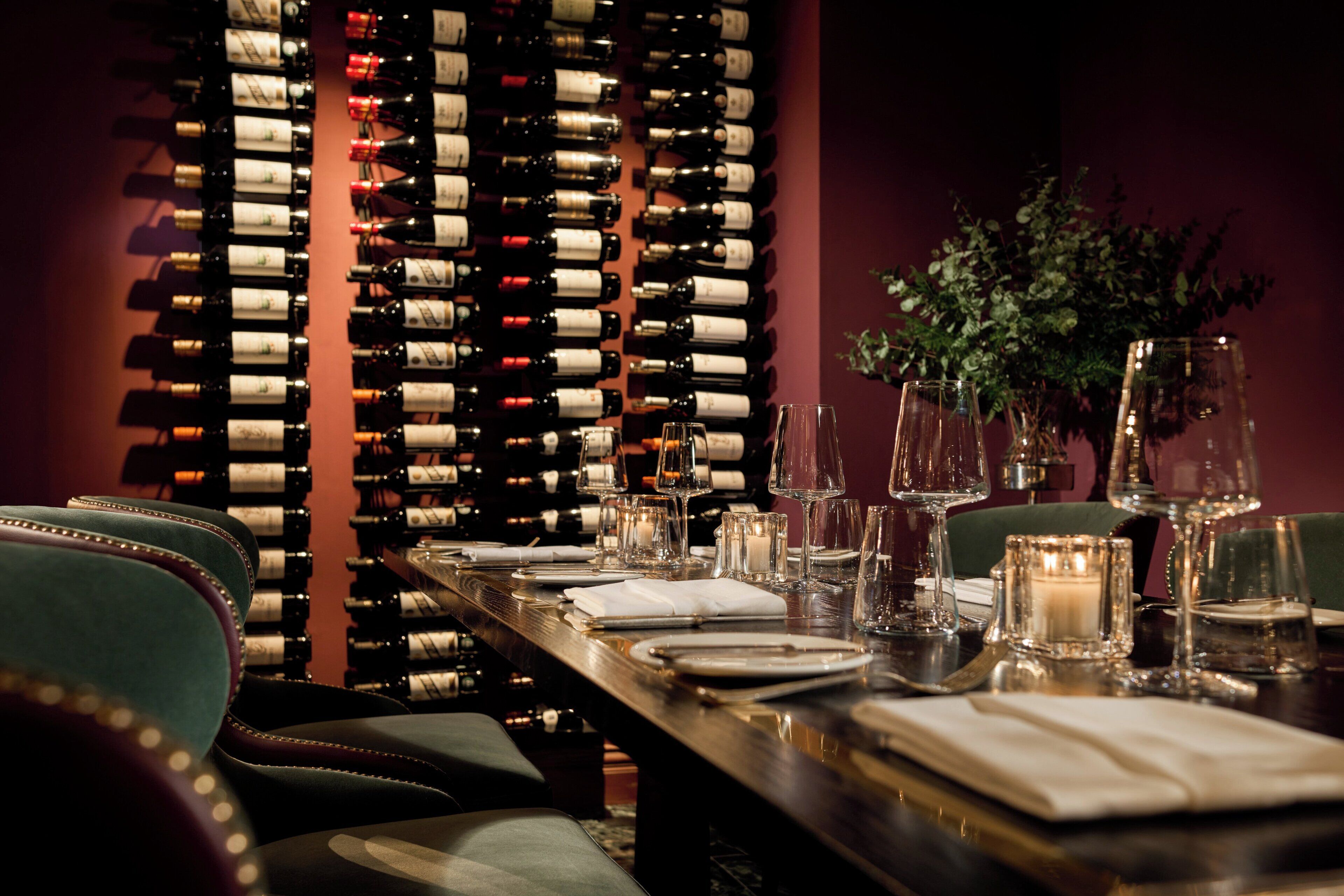 A dining table set with wine glasses, plates, and a candle, with a wine rack in the background.