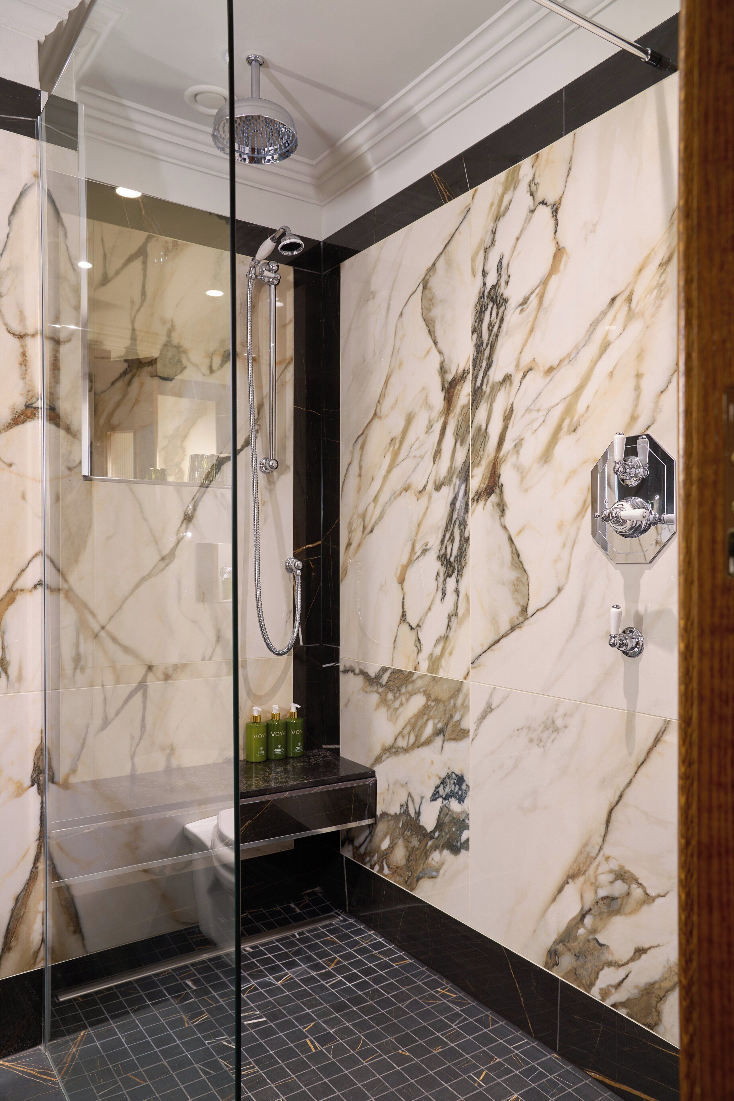 A modern bathroom with a glass-enclosed shower, marble walls, and a black tiled floor.