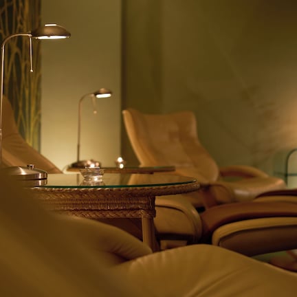 A cozy seating area with leather chairs and a glass table, accompanied by two floor lamps and a lit candle on a side table.