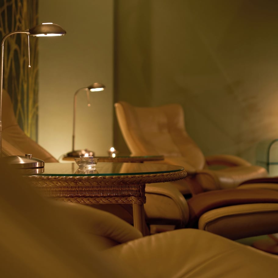 A cozy seating area with leather chairs and a glass table, accompanied by two floor lamps and a lit candle on a side table.