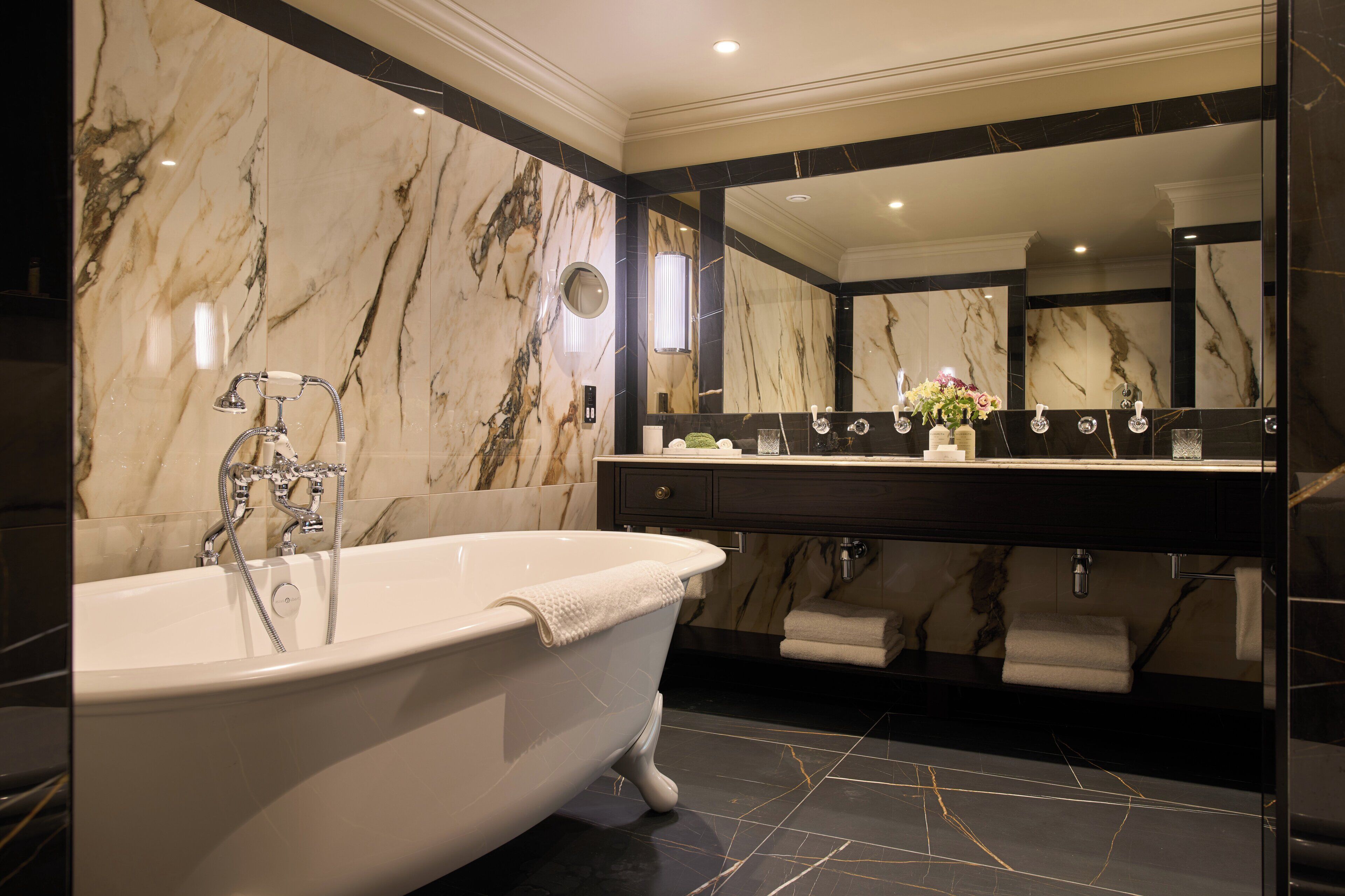 Une salle de bain avec une baignoire sur pieds, un grand miroir et un mur en marbre.