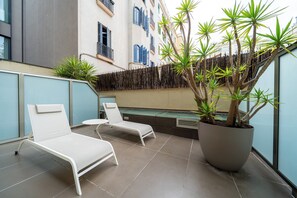A balcony with two white lounge chairs, a large potted plant, and a bamboo fence. - Hotel Constanza (Barcelona)