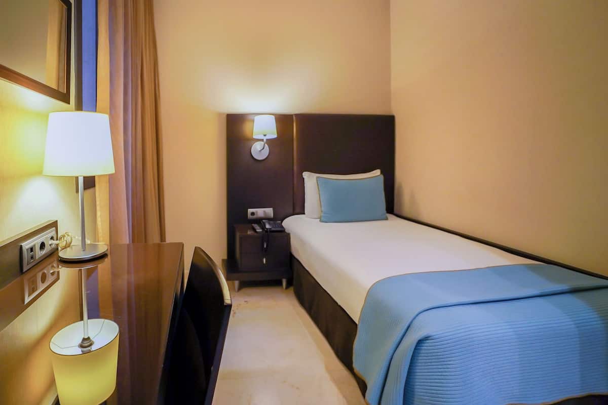 Una habitación de hotel con cama, mesita de noche, lámpara y velador.