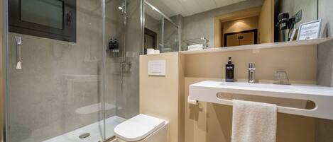 A modern bathroom with a glass-enclosed shower, a white toilet, a sink with a towel hanging on the wall, and a trash bin.