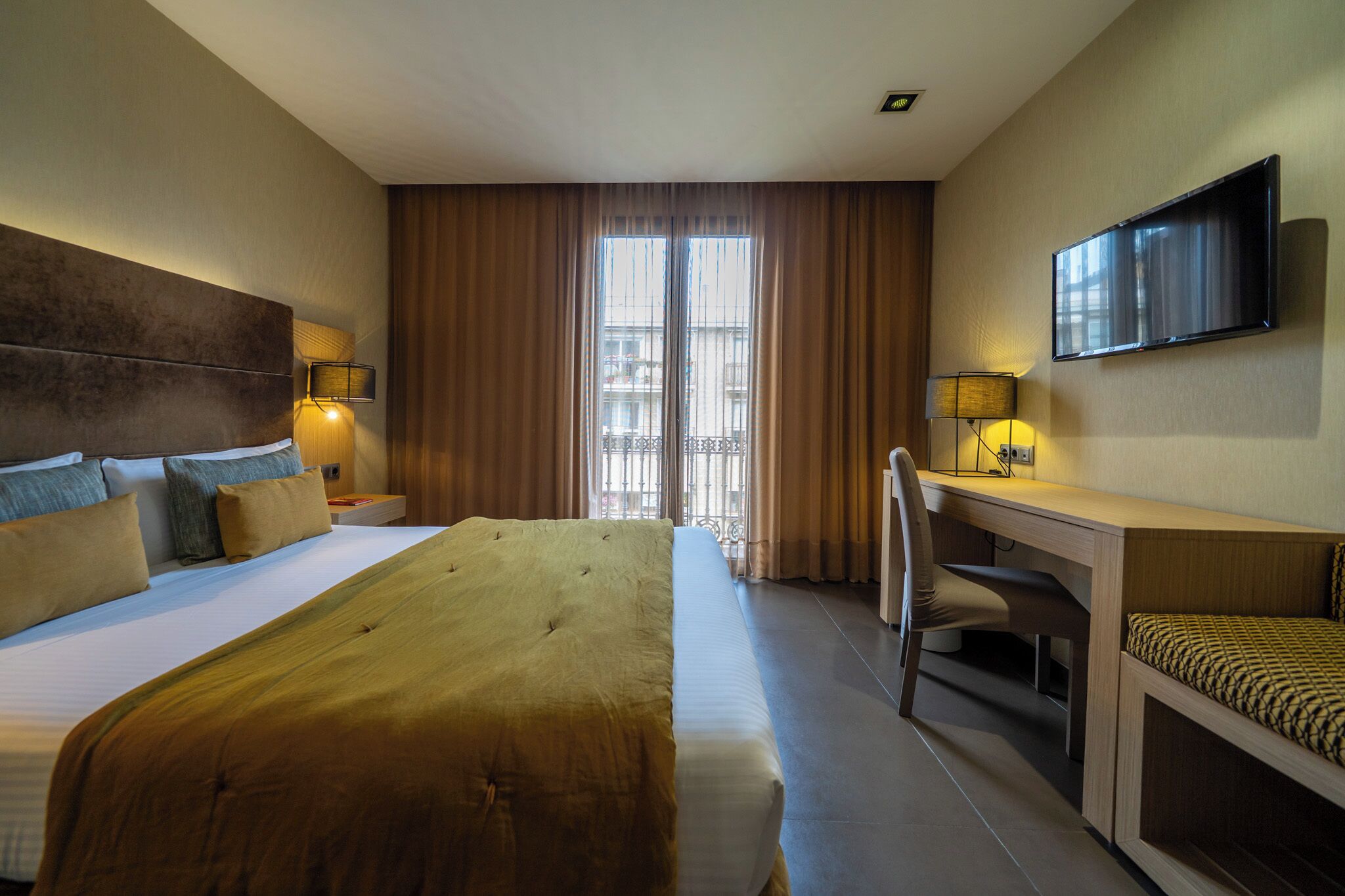 A hotel room with a large bed, a desk with a chair, a television, and a window with curtains.
