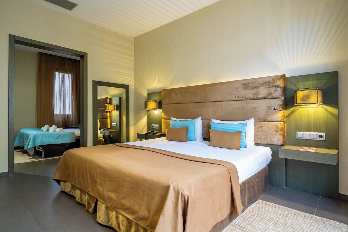 Habitación de hotel con una cama grande, dos mesitas de noche, un espejo y una ventana con cortinas.