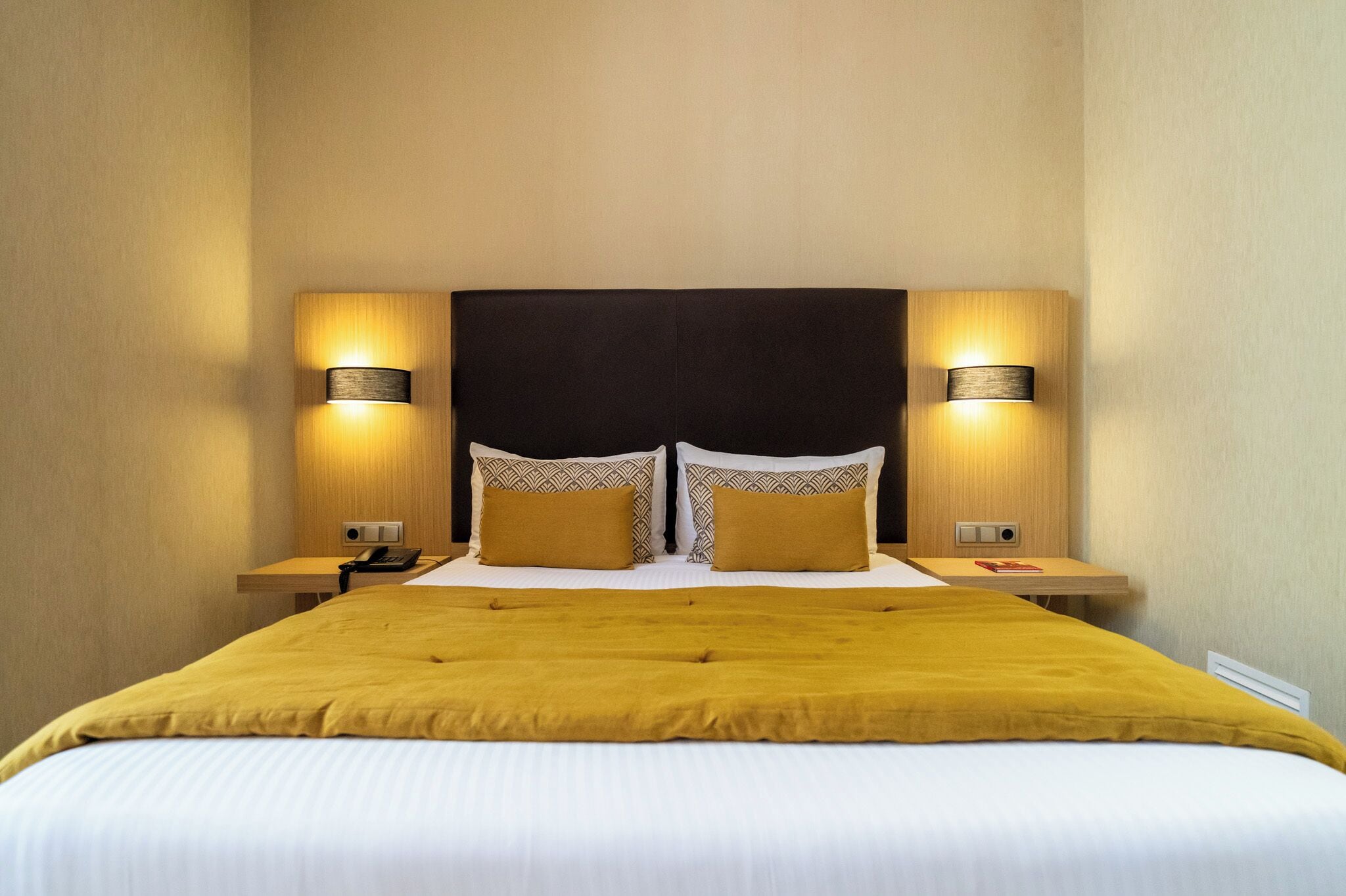A hotel room with a large bed, two bedside tables, and two wall-mounted lamps.