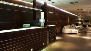 A modern reception area with a long counter, computers, and a seating area with sofas. - Hotel Constanza (Barcelona)