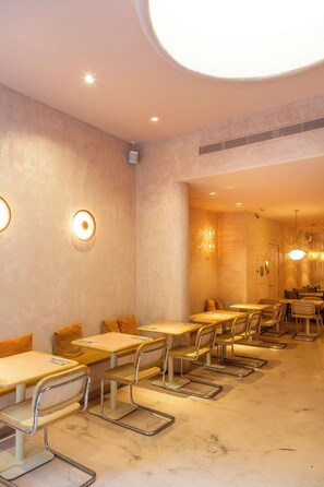 A modern dining area with round tables and metal chairs, recessed ceiling lighting, and a marble floor. - Hotel Constanza (Barcelona)