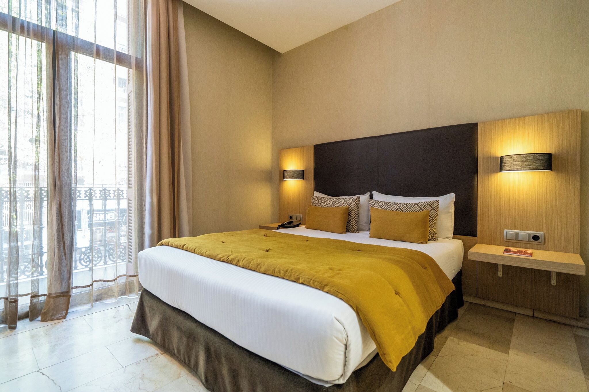 A hotel room with a large bed, two bedside lamps, a nightstand, and a window with curtains.