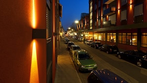 Vista nocturna de una calle con coches aparcados y edificios con ventanas iluminadas.
