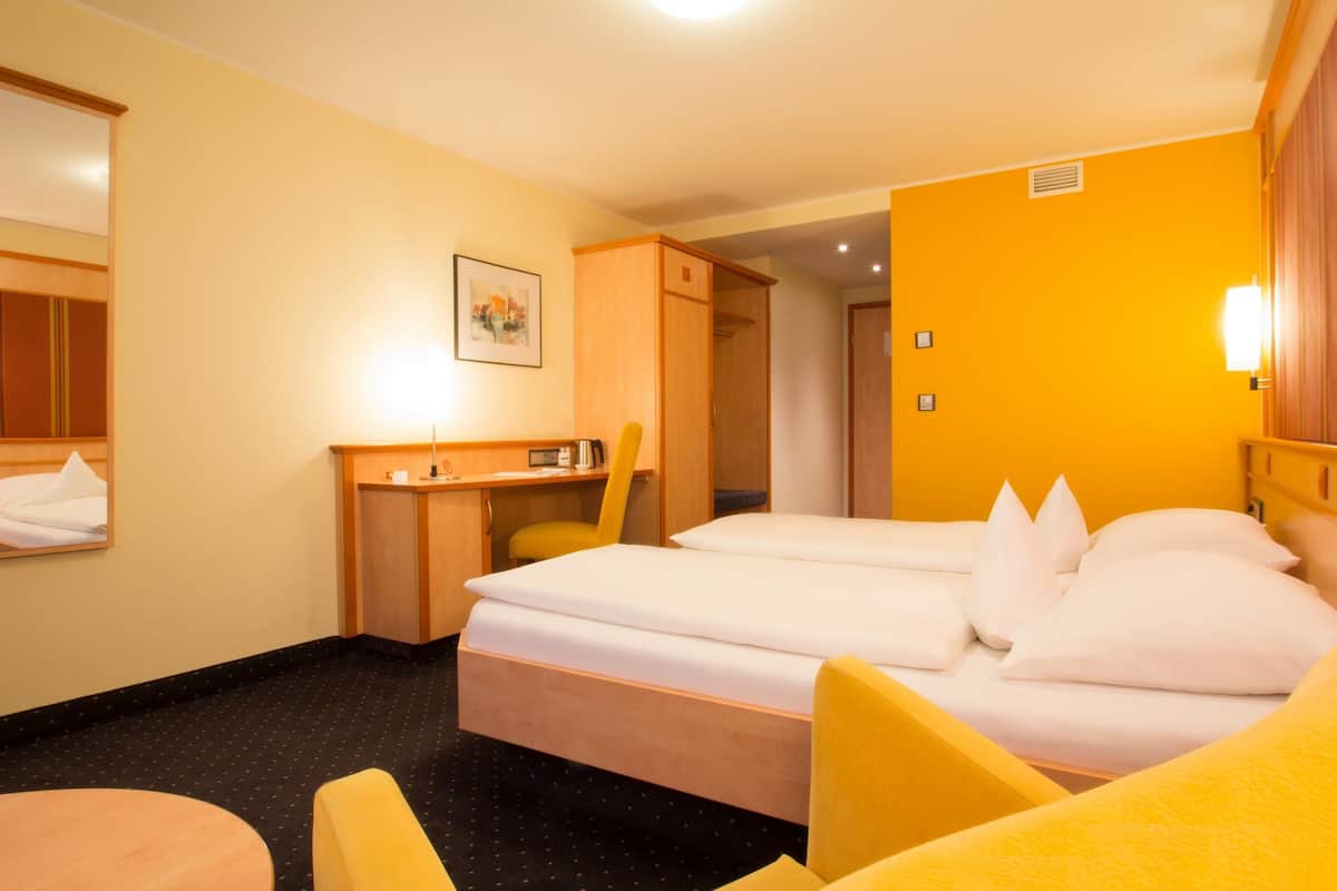 A hotel room with a bed, a desk, a chair, and a small table.