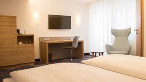 Una habitación de hotel con cama, escritorio con silla, televisor y armario.