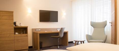 A hotel room with a bed, a desk with a chair, a television, and a wardrobe.