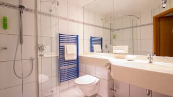 Et moderne badeværelse med en glasbrusekabine, et hvidt toilet og en vask med spejl.