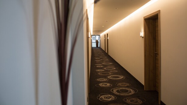 Un pasillo con alfombra estampada y una puerta de madera al final.