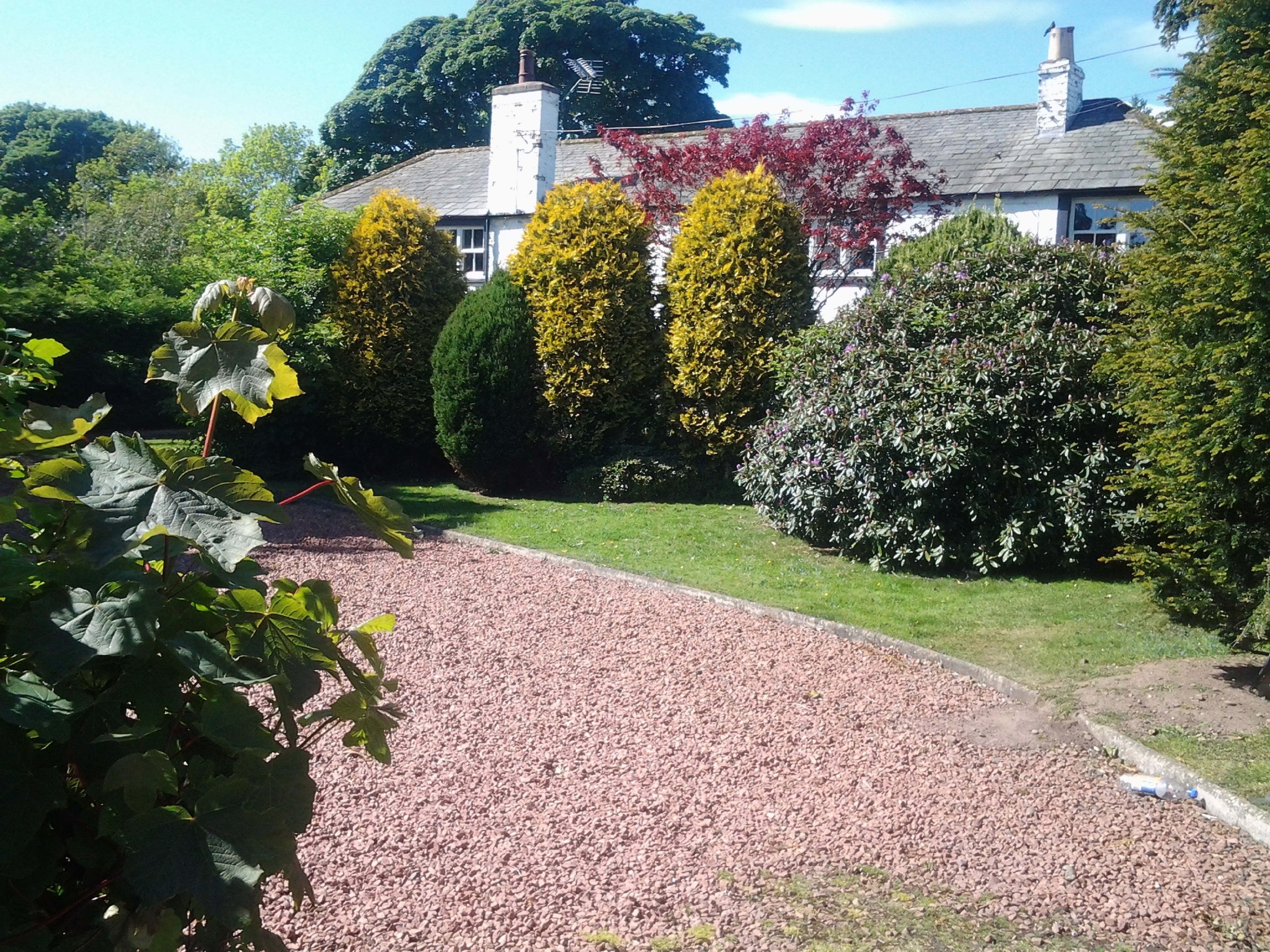 A gravel driveway leading to a house with a white exterior and a chimney.