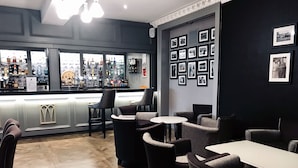 A bar area with a counter displaying various bottles, a selection of chairs, and a wall adorned with framed pictures.