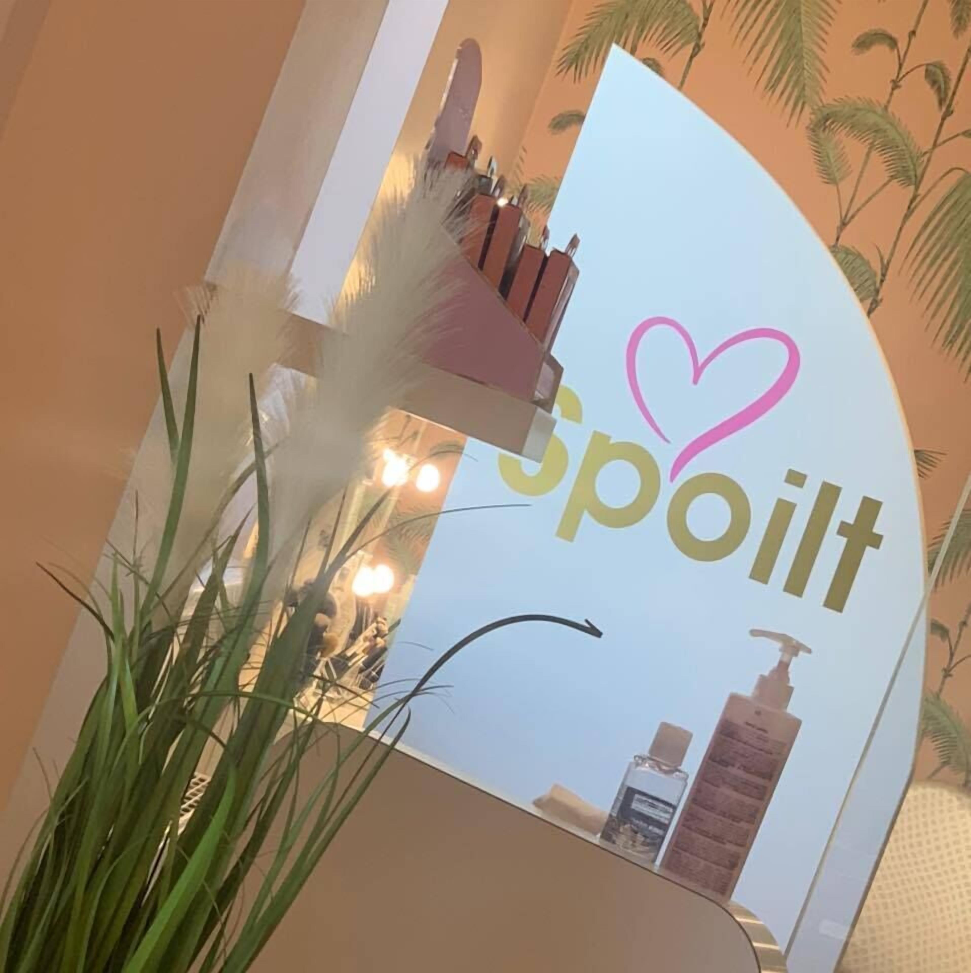 Un espejo refleja un espacio de spa con un letrero que dice 'SPOILT' y un símbolo de corazón.