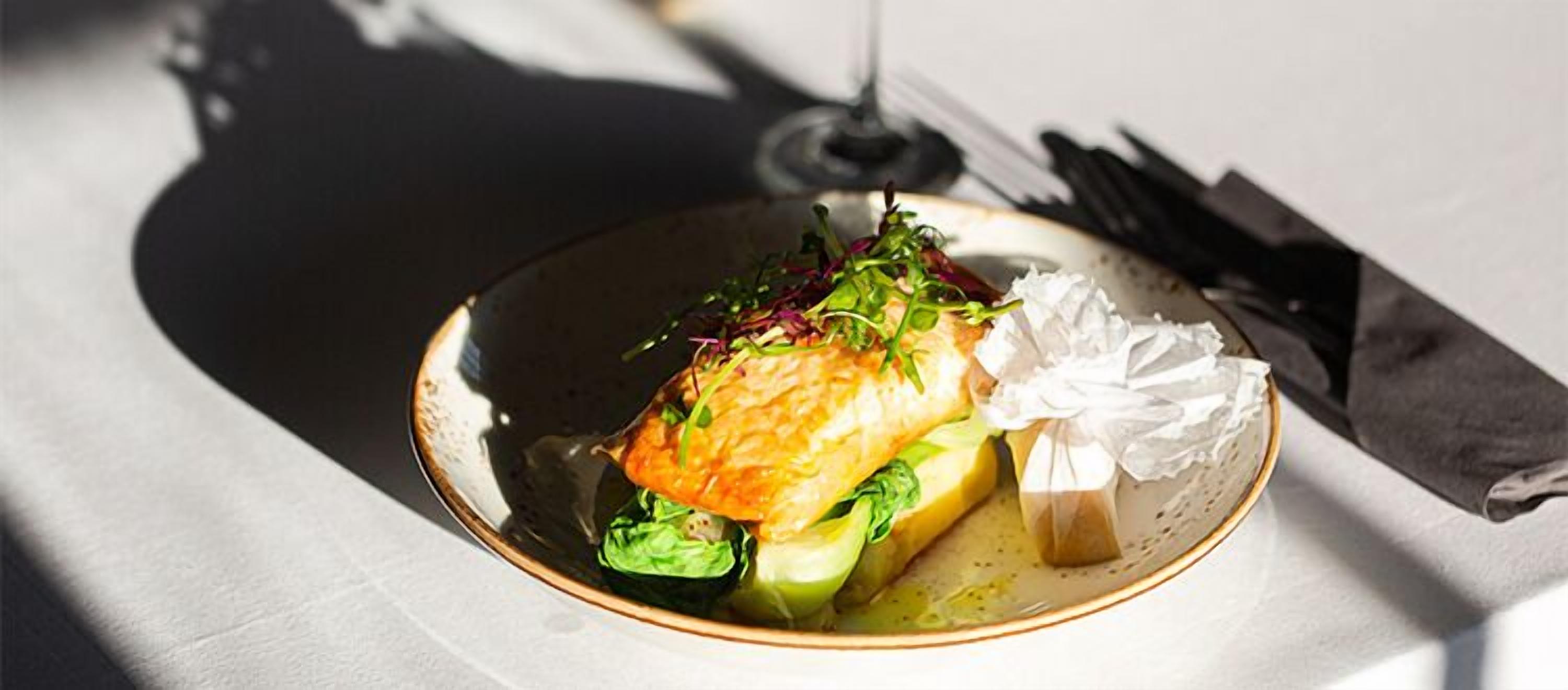 Un plato con un trozo de salmón, vegetales verdes y un pedazo de pan sobre una mesa.