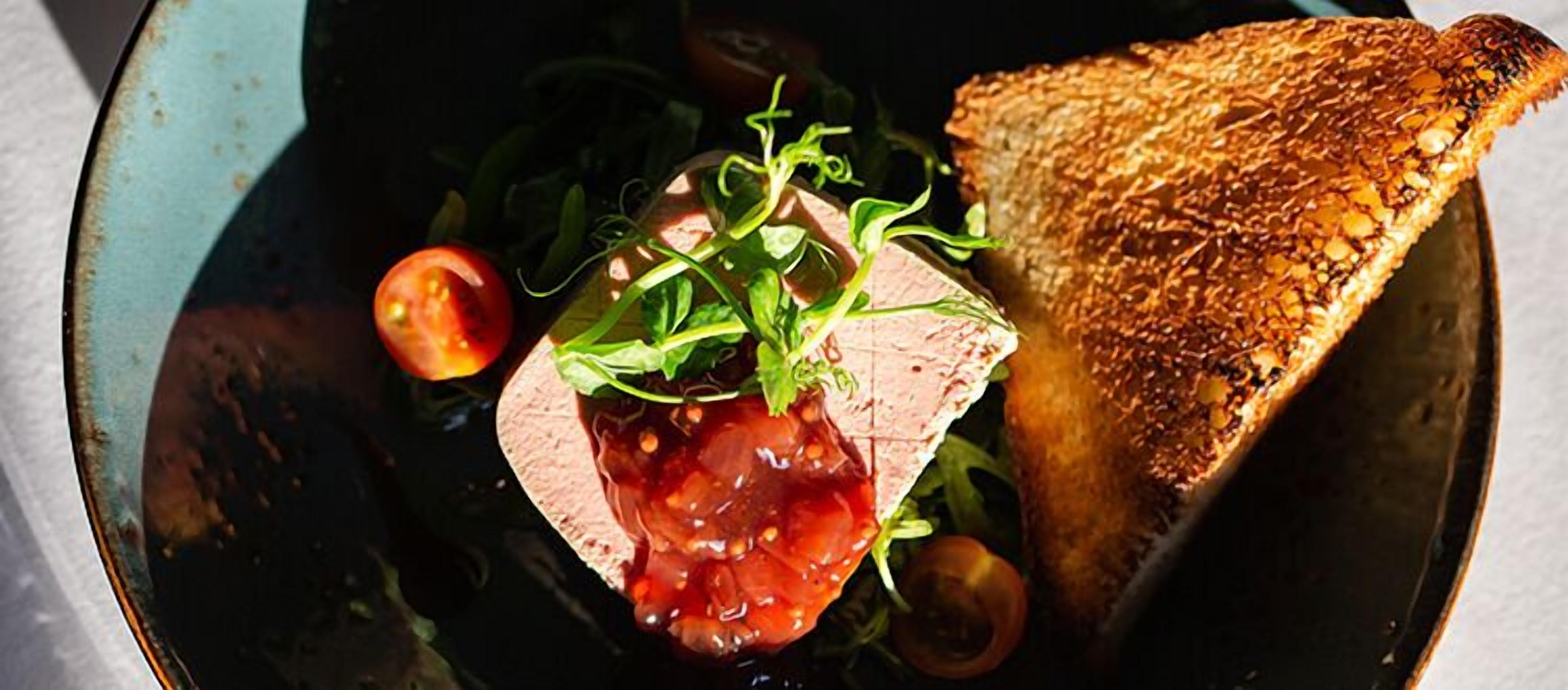 Un sándwich con rebanada de pan tostado, lechuga, tomate y una hamburguesa, servido en un recipiente oscuro.