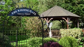 A gazebo with a sign reading "The Kissing Gate Gretna Green" surrounded by lush greenery and a wooden fence.