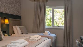 A hotel room with two beds, a window with curtains, a headboard, and a bedside lamp.