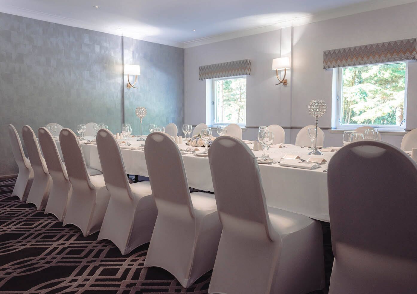 A conference room with a long table, white chairs, and windows with curtains.