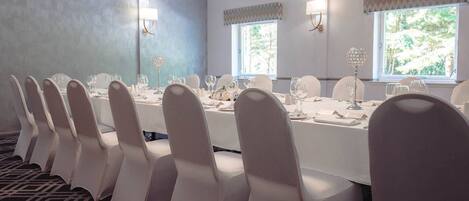 A conference room with a long table, white chairs, and windows with curtains.