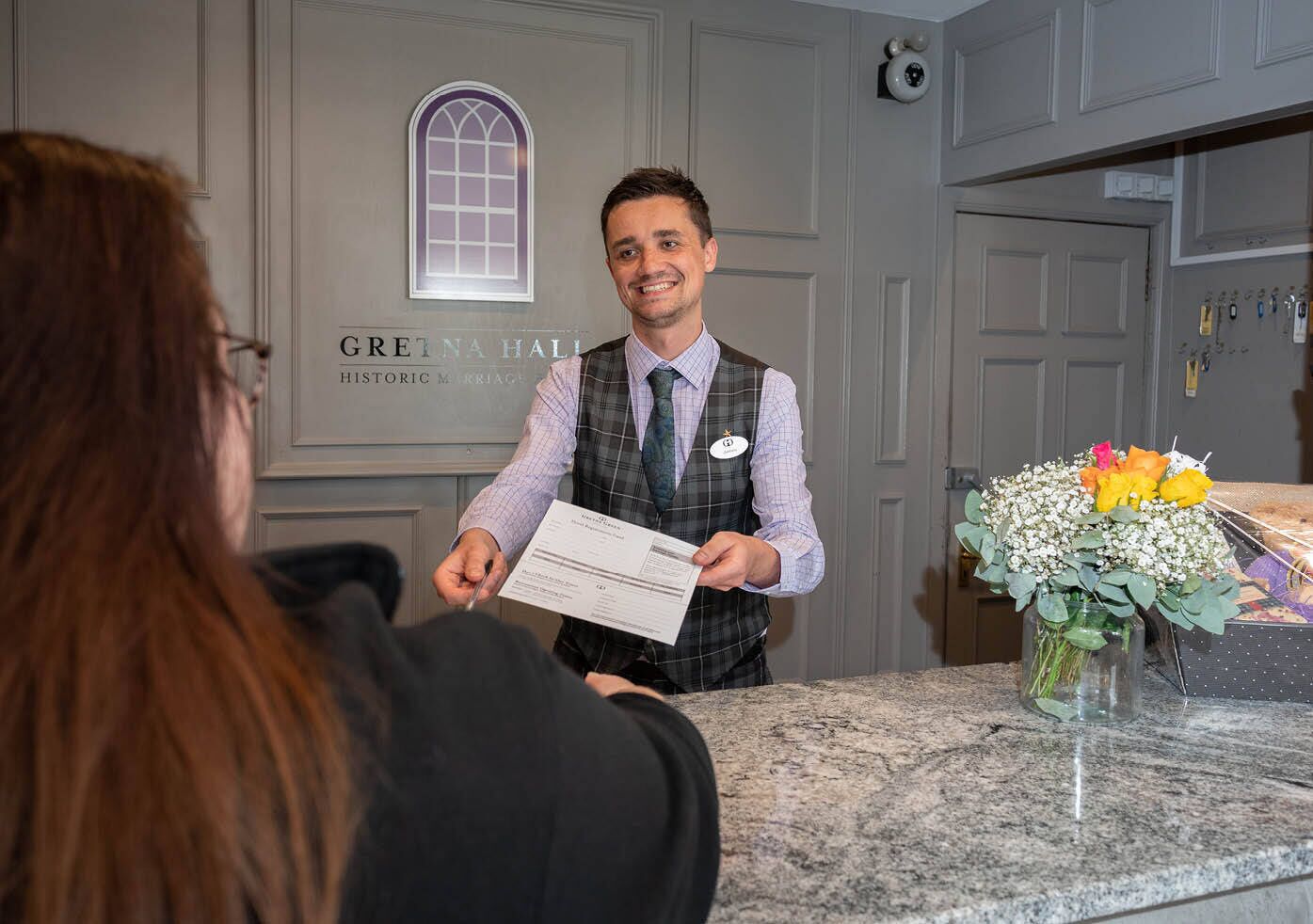 A hotel reception area with a marble counter, a nameplate, and a bouquet of flowers.