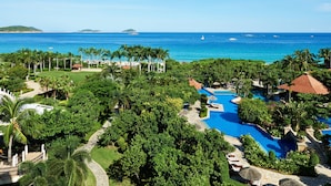 Een resort met een groot zwembad, weelderige begroeiing en uitzicht op de oceaan.