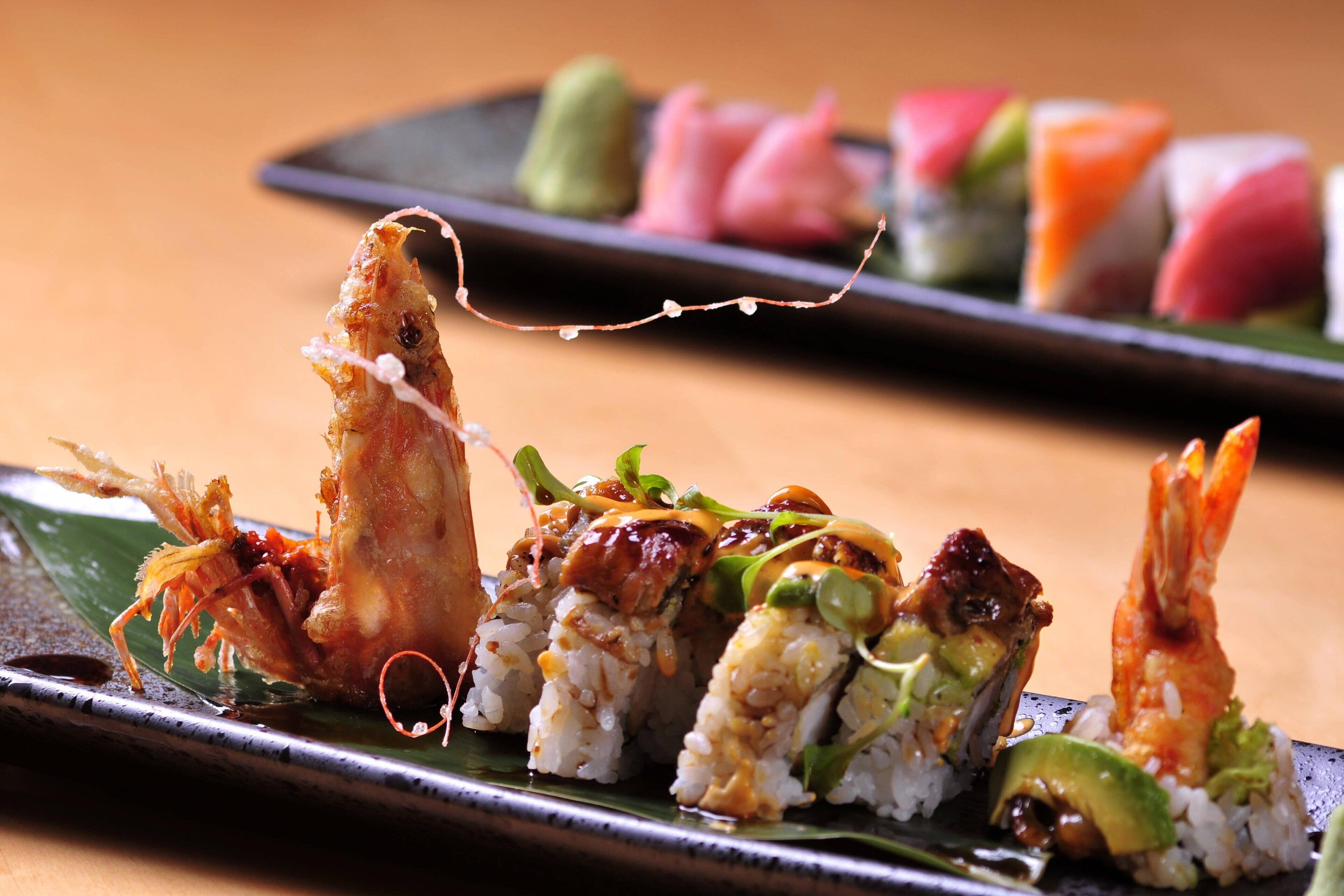 Variedad de platos de sushi sobre un plato negro, con una hoja verde debajo.