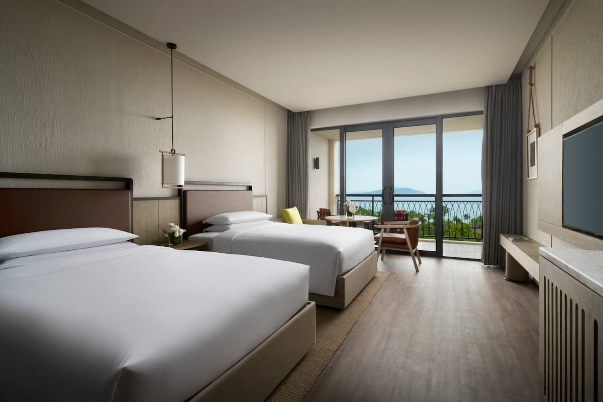 Une chambre d’hôtel avec deux lits, une télévision, un balcon donnant sur la mer et un coin repas.