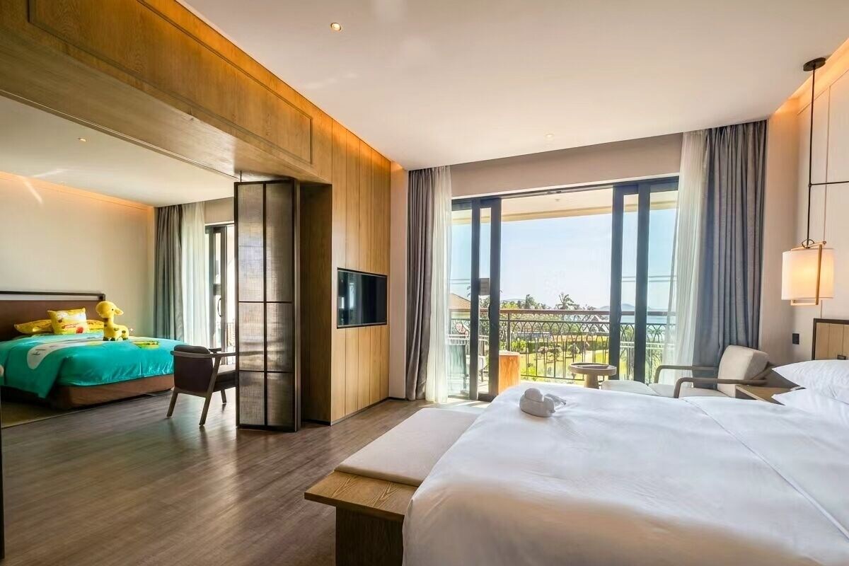 Quarto de hotel com uma cama grande, área de estar, televisão e varanda com vista.