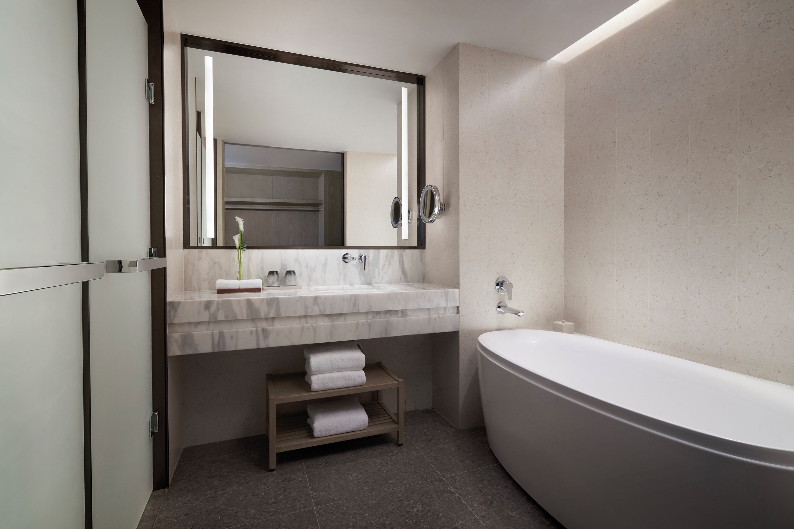 A modern bathroom with a large bathtub, a marble sink, and a mirror with integrated lighting.