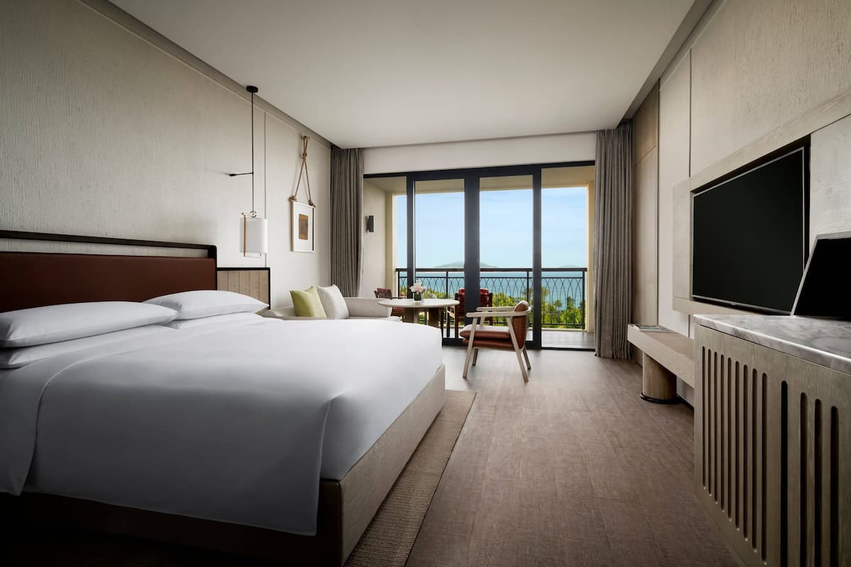 Une chambre d’hôtel avec un grand lit, un coin repas avec une table et des chaises, une télévision et un balcon avec vue.