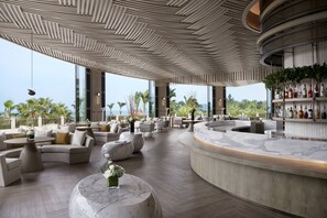 Een moderne lounge met een gebogen bar, comfortabele zithoek en grote ramen met uitzicht op zee.